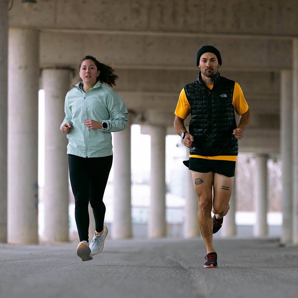A man and woman running together under an underpass wearing Garmin Forerunner 955 watches