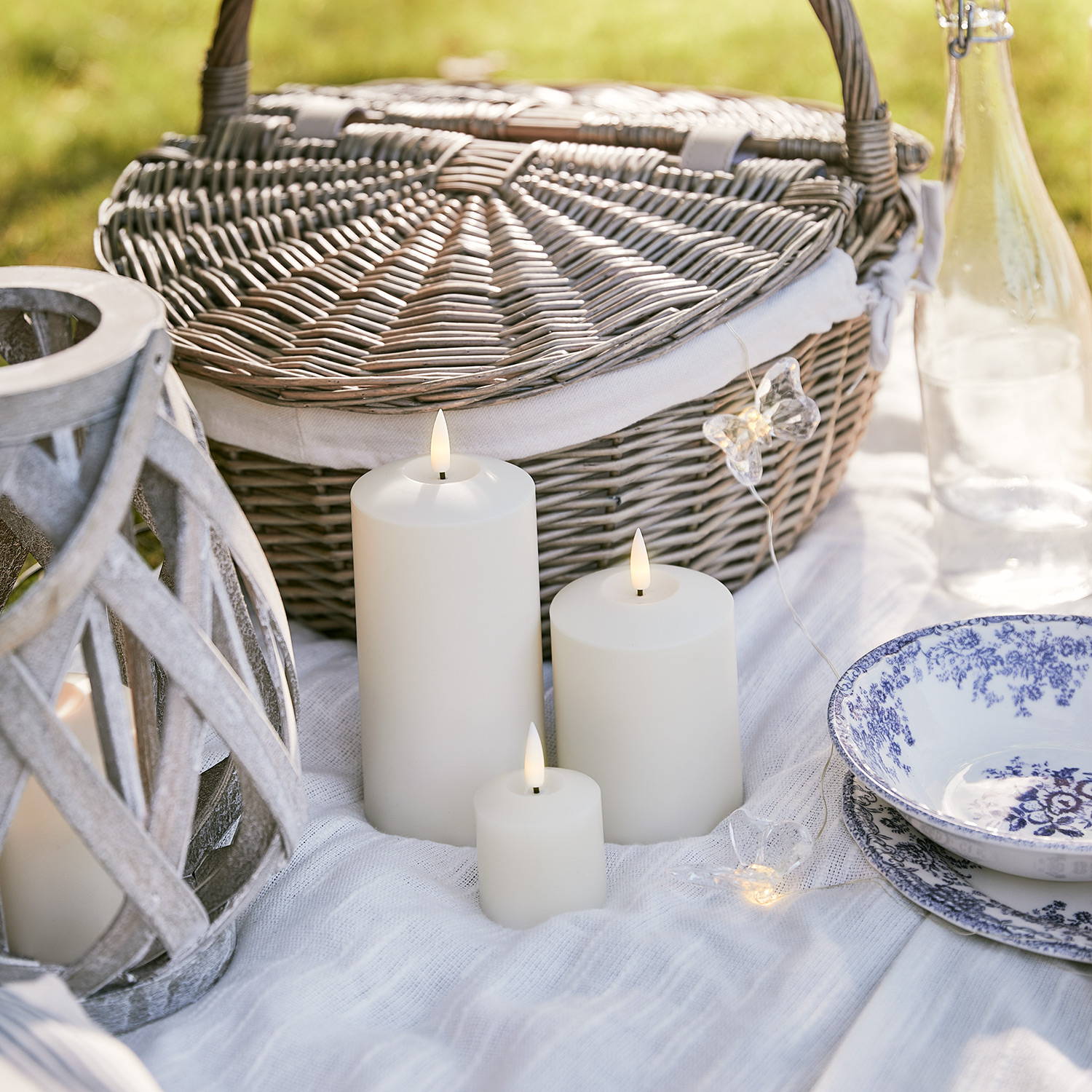 A summer picnic setting with a wooden lantern, picnic basket, LED candles and butterfly fairy lights.