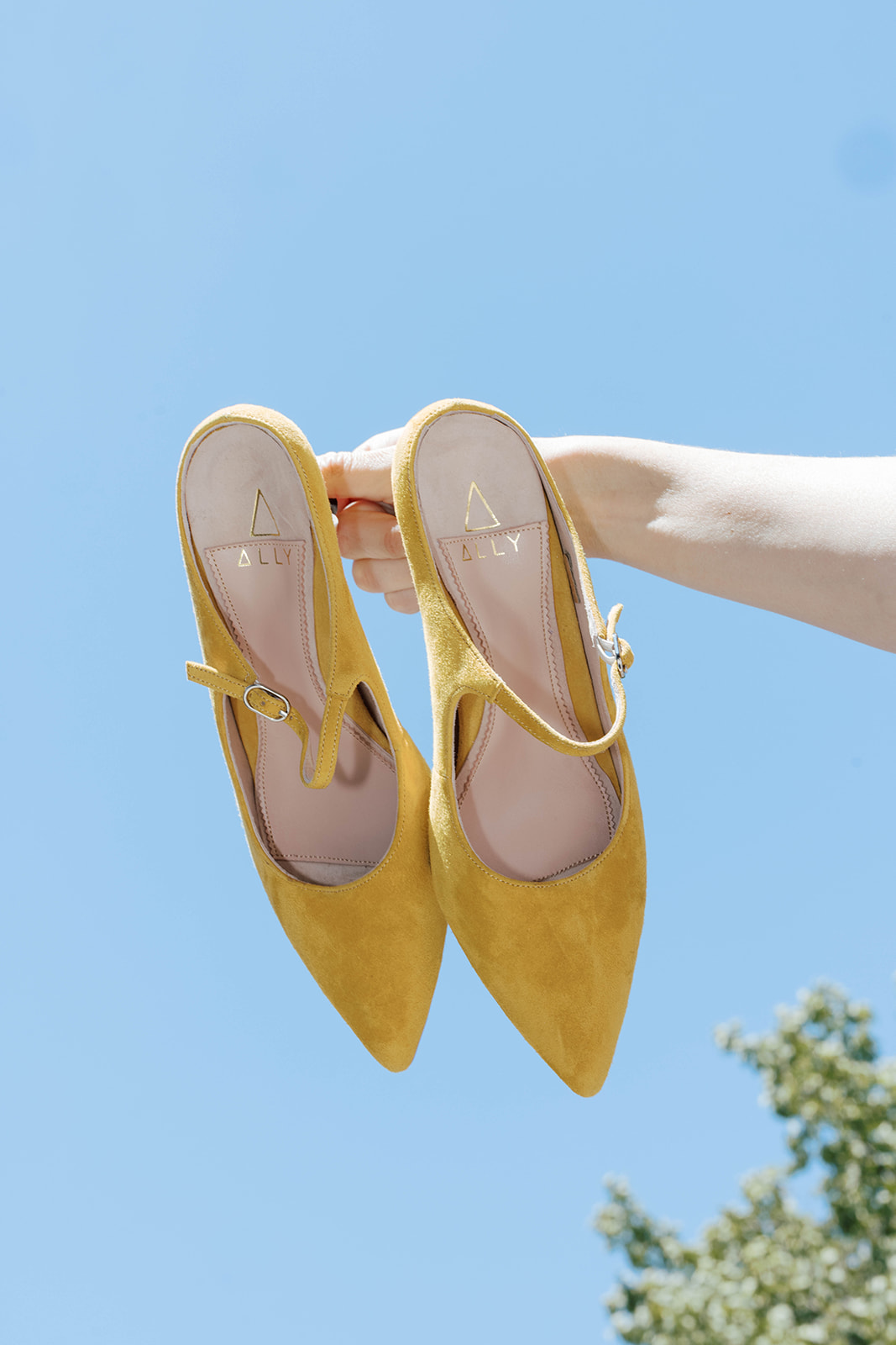 A pair of yellow shoes held against a blue sky.