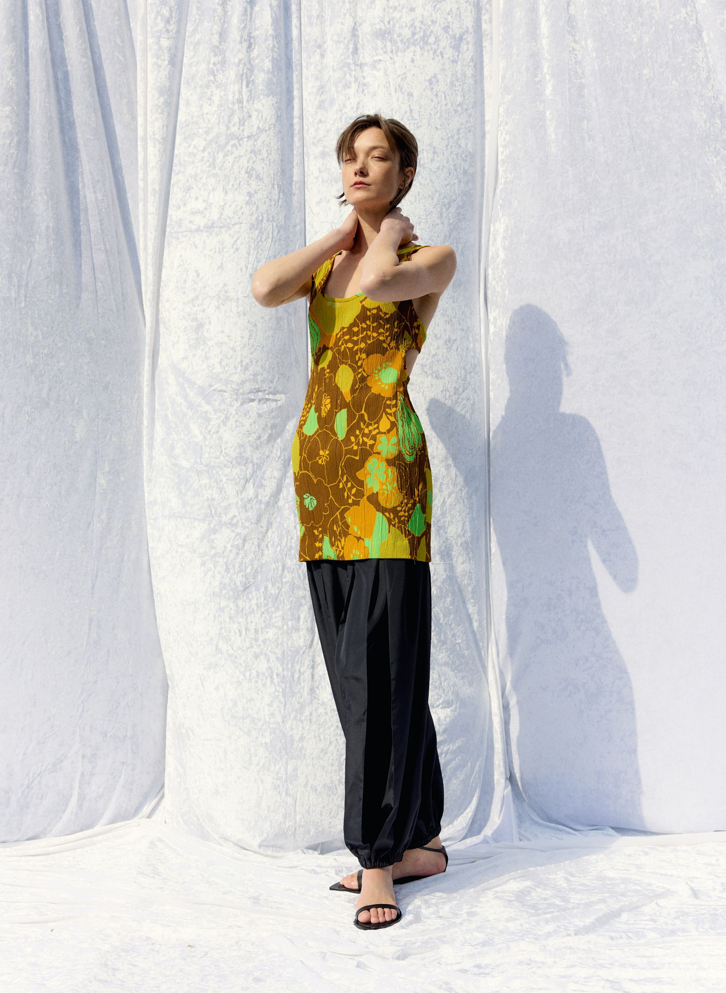 Model wearing a patterned top and black pants, posing against a white backdrop.