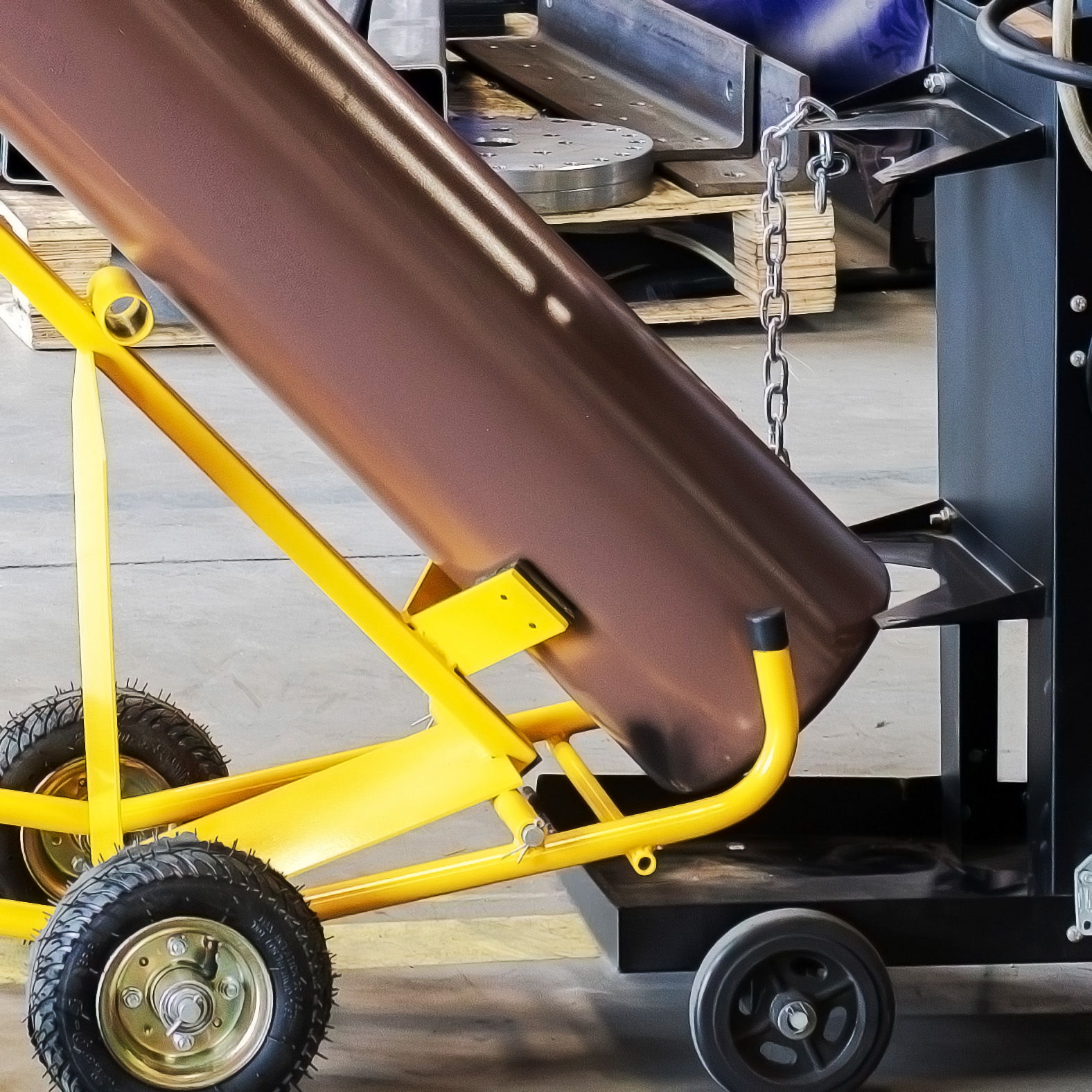 A yellow and black cart holding a brown cylindrical object in an industrial setting.