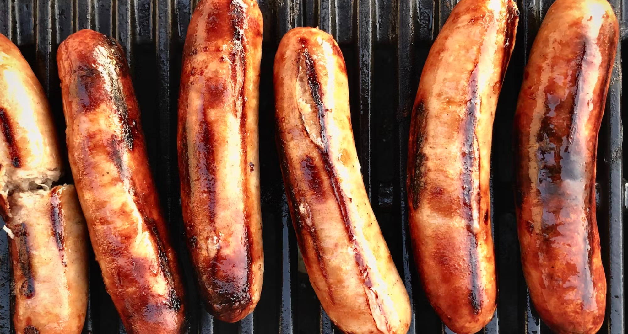 six sausages lined up on a grill