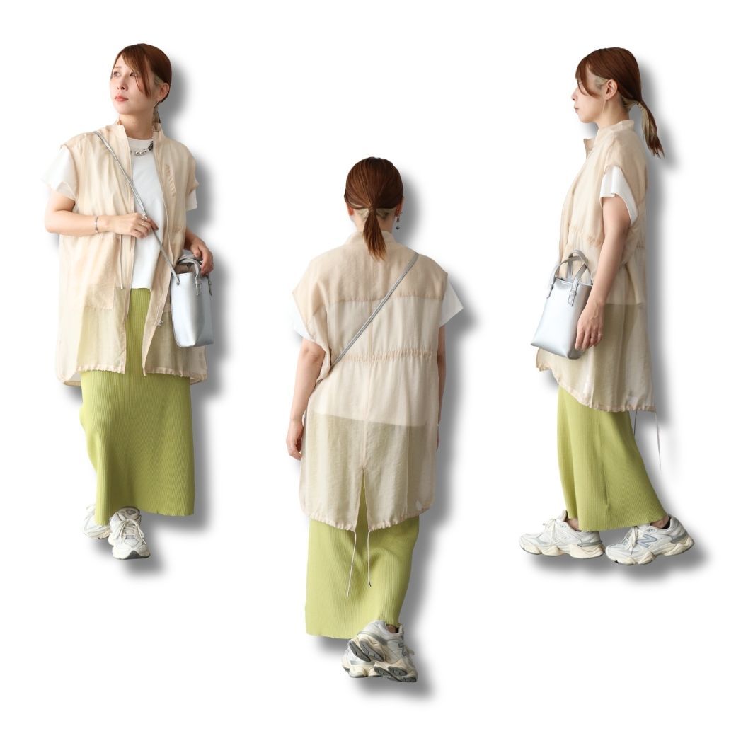 A woman in a stylish outfit, featuring a long vest and green skirt.