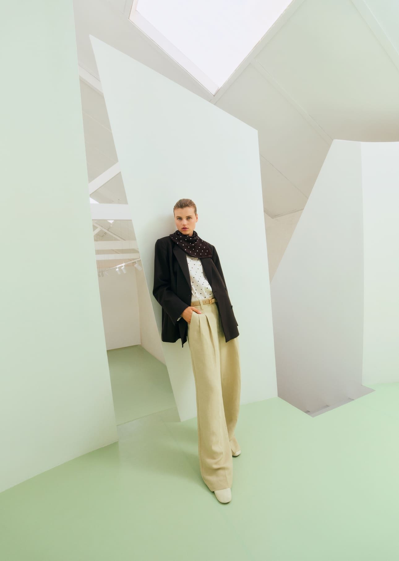 A person in stylish attire stands in a modern, minimalist space.