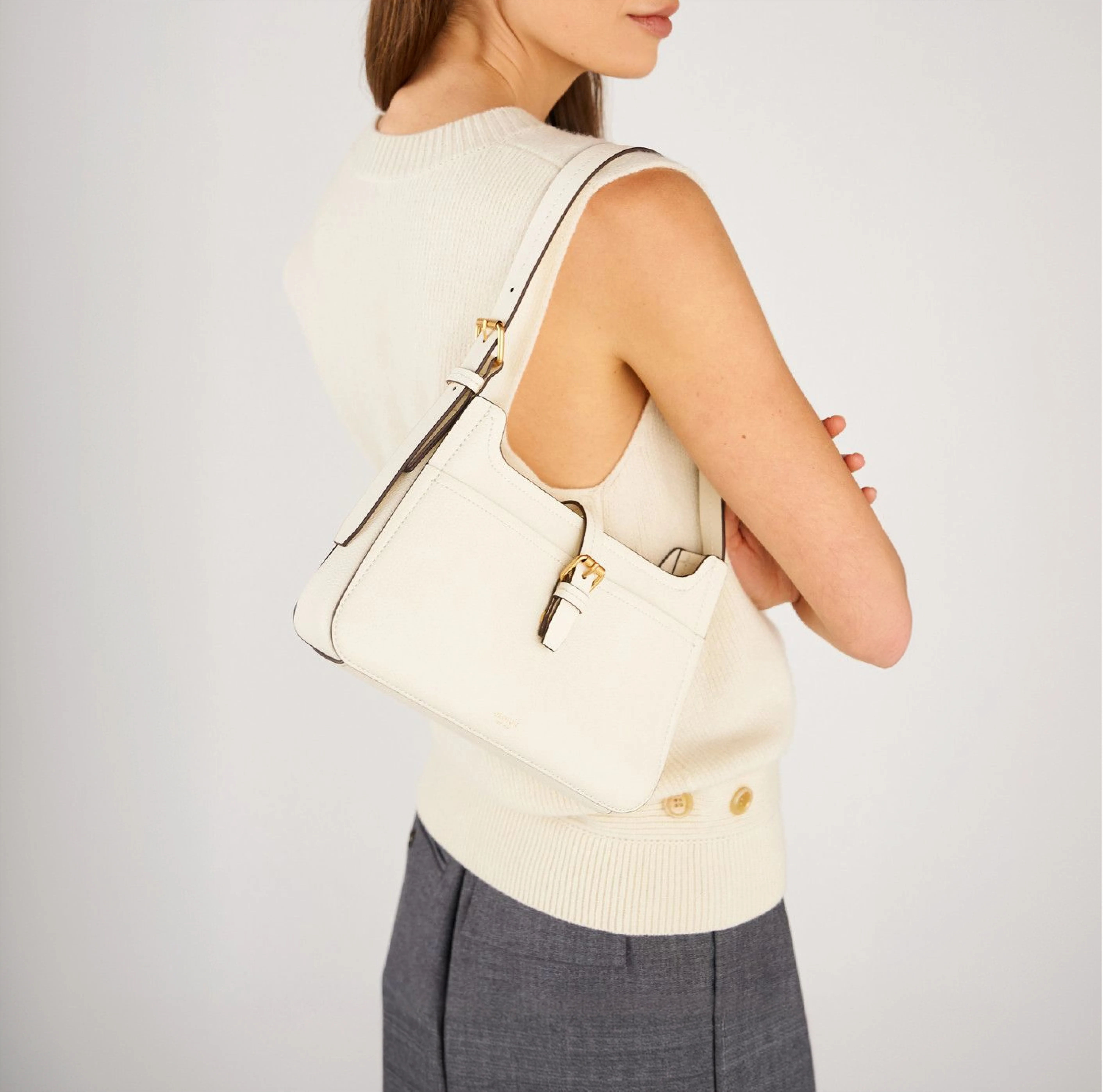 A woman wearing a cream sweater holding a white handbag on her shoulder.