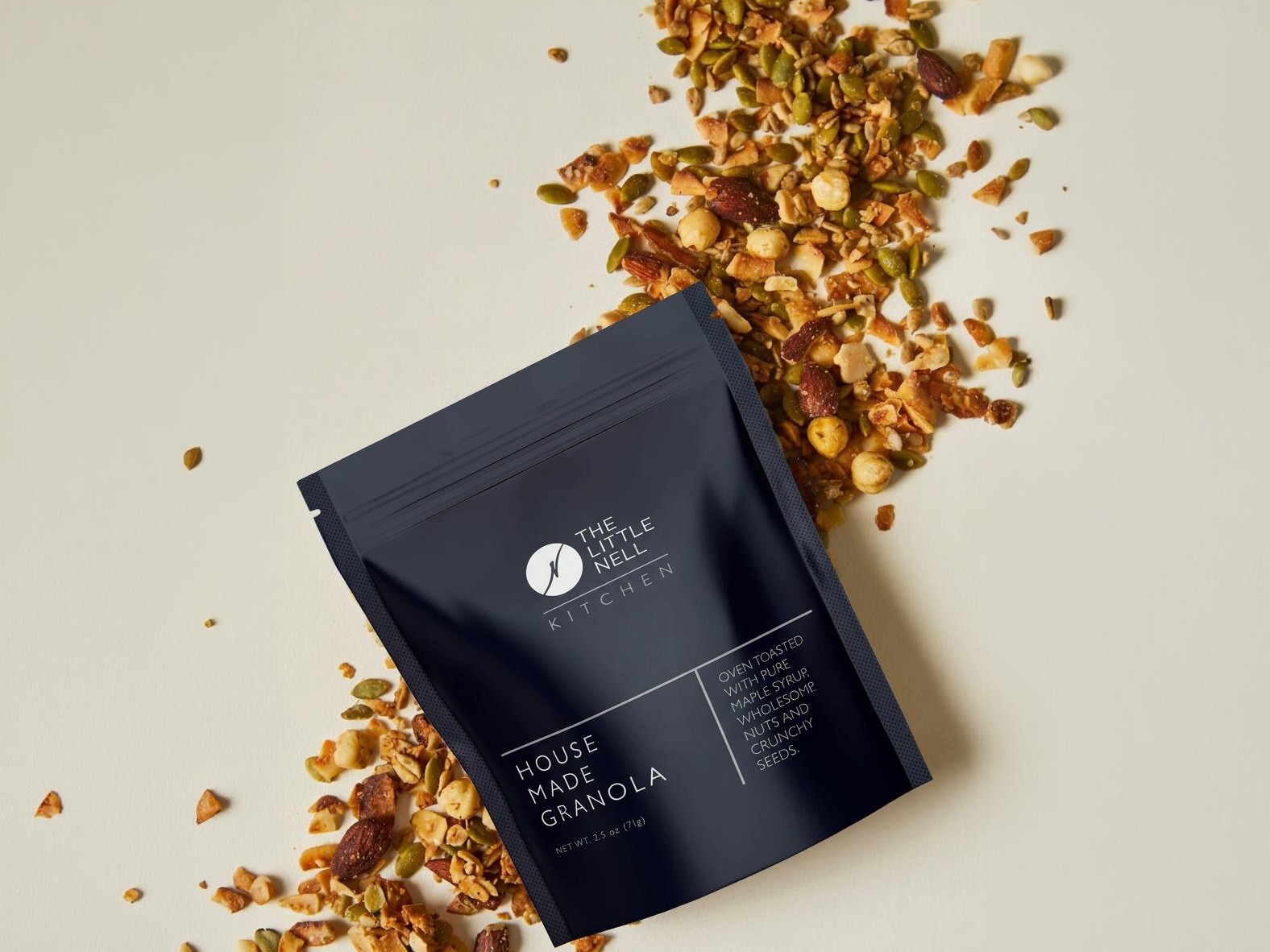 A black snack package with granola scattered around it on a light background.