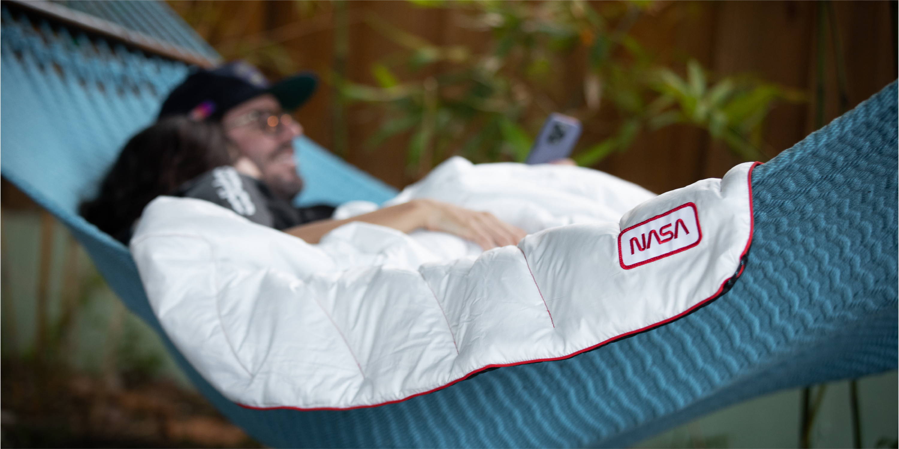 Couple laying in a hammock with a white NASA worm logo blanket by Rumpl