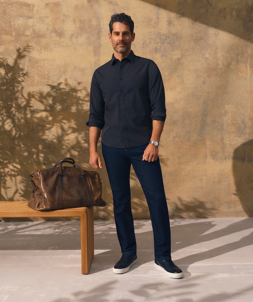 Man in casual outfit standing next to a brown bag on a bench.