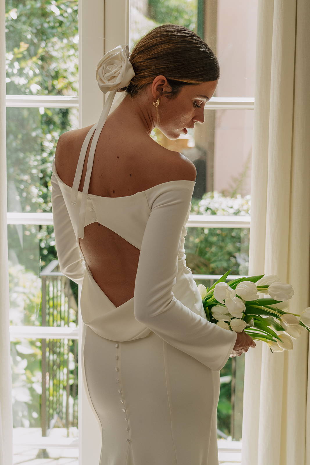 the back of a woman standing in a window wearing the Deia gown