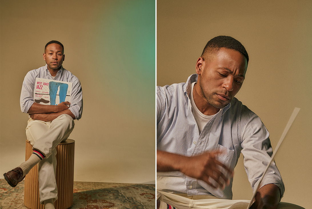 Man sitting on a box, reading a book, with a neutral background.