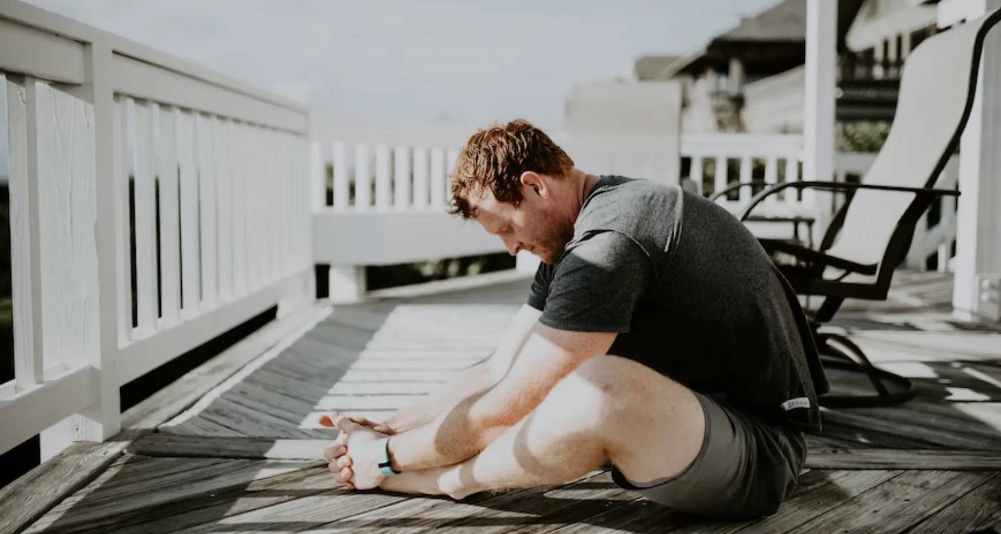 man in all gray doing a sitting yoga pose on a weathered deck