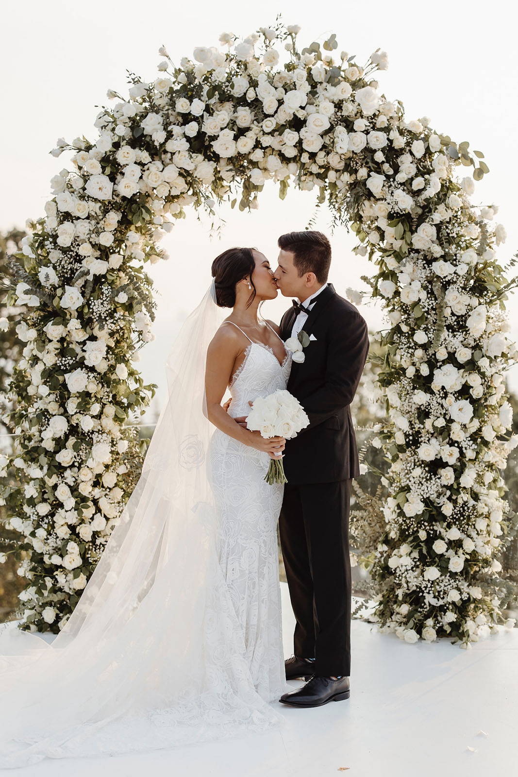 Bride and groom with white floral arched arbor