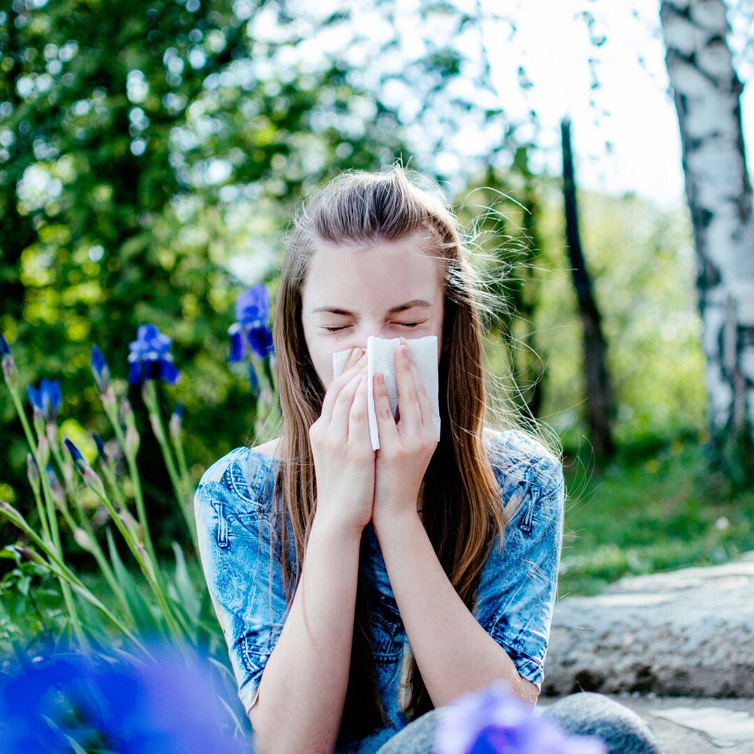 Teenager blowing her nose – it’s sunny and there are birch trees behind her so maybe she has pollen allergy