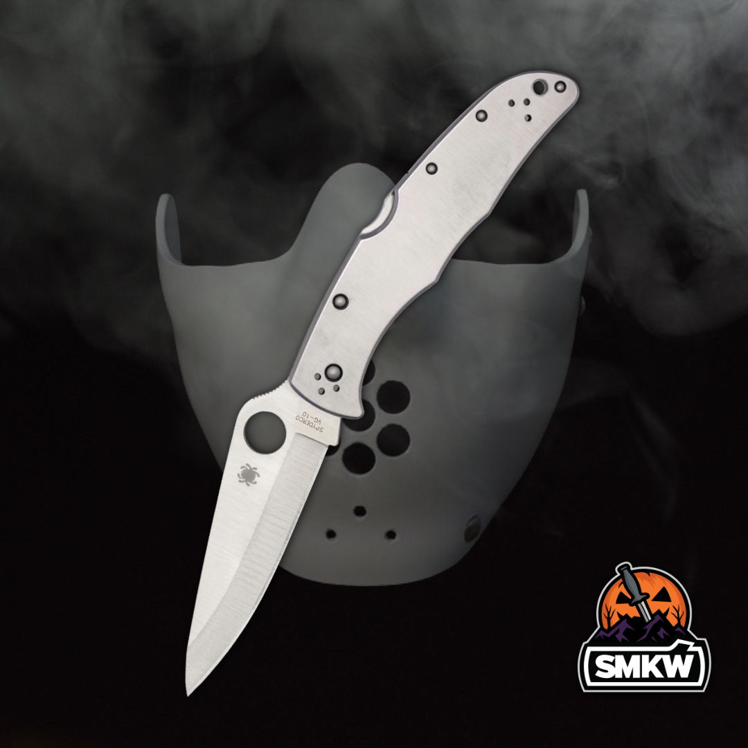 A silver folding knife against a dark, smoky background with a mask.