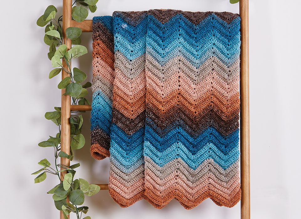 A colorful chevron-patterned blanket draped over a wooden ladder with greenery.