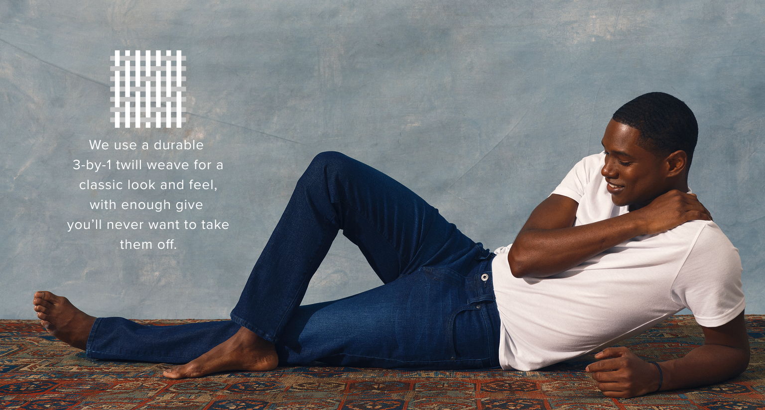 A man lying on a rug, wearing a white shirt and blue jeans.