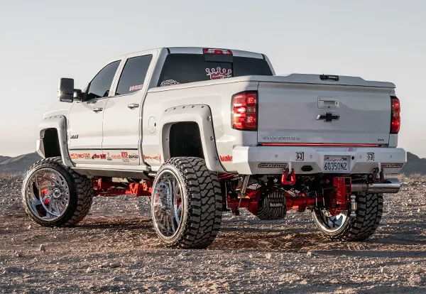 Rear three-quarter view of Juan's lifted white 2018 Chevy Silverado 2500HD with red suspension and oversized chrome wheels, install photo 4