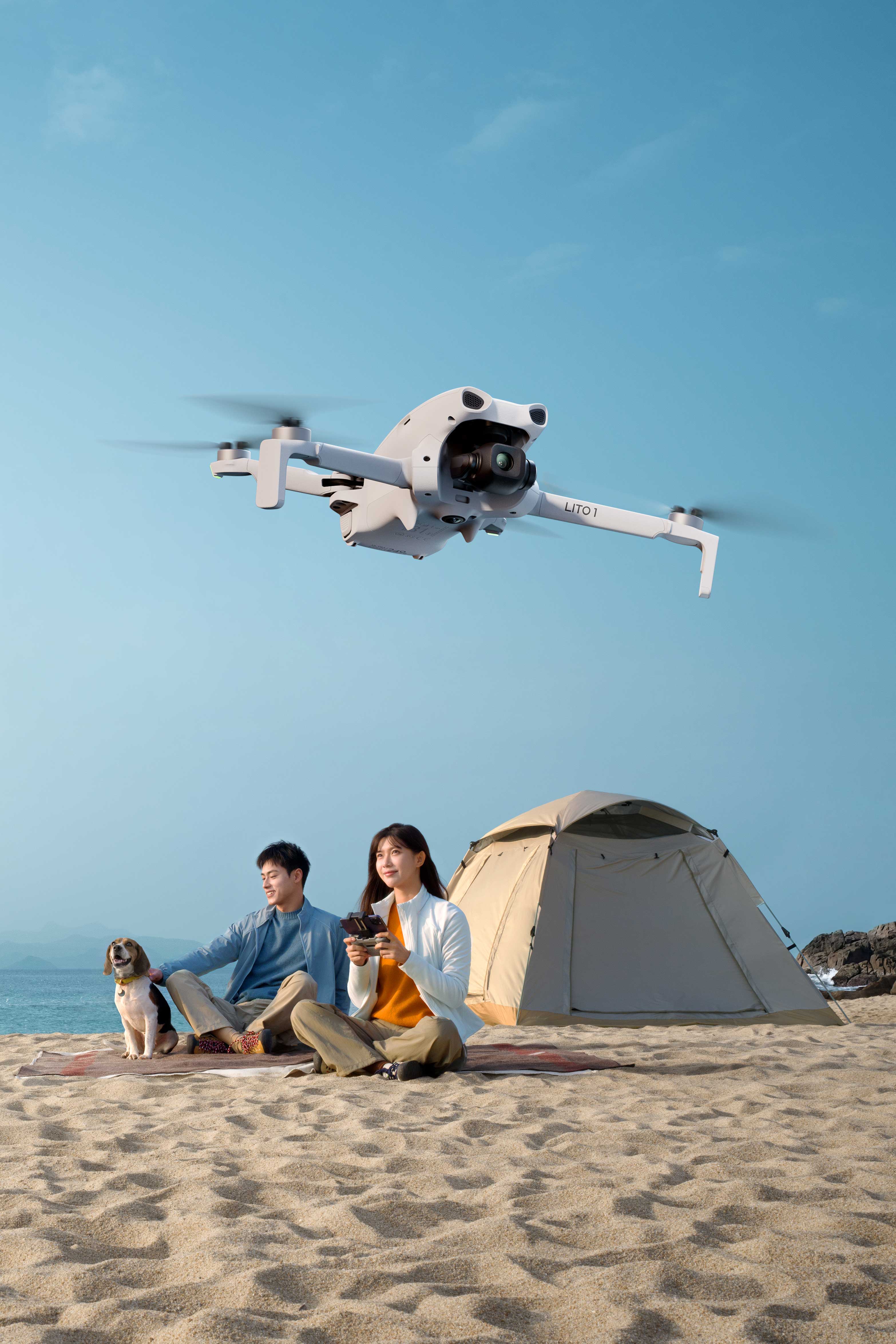A couple sits on the beach with a DJI Lito 1 drone flying above them.