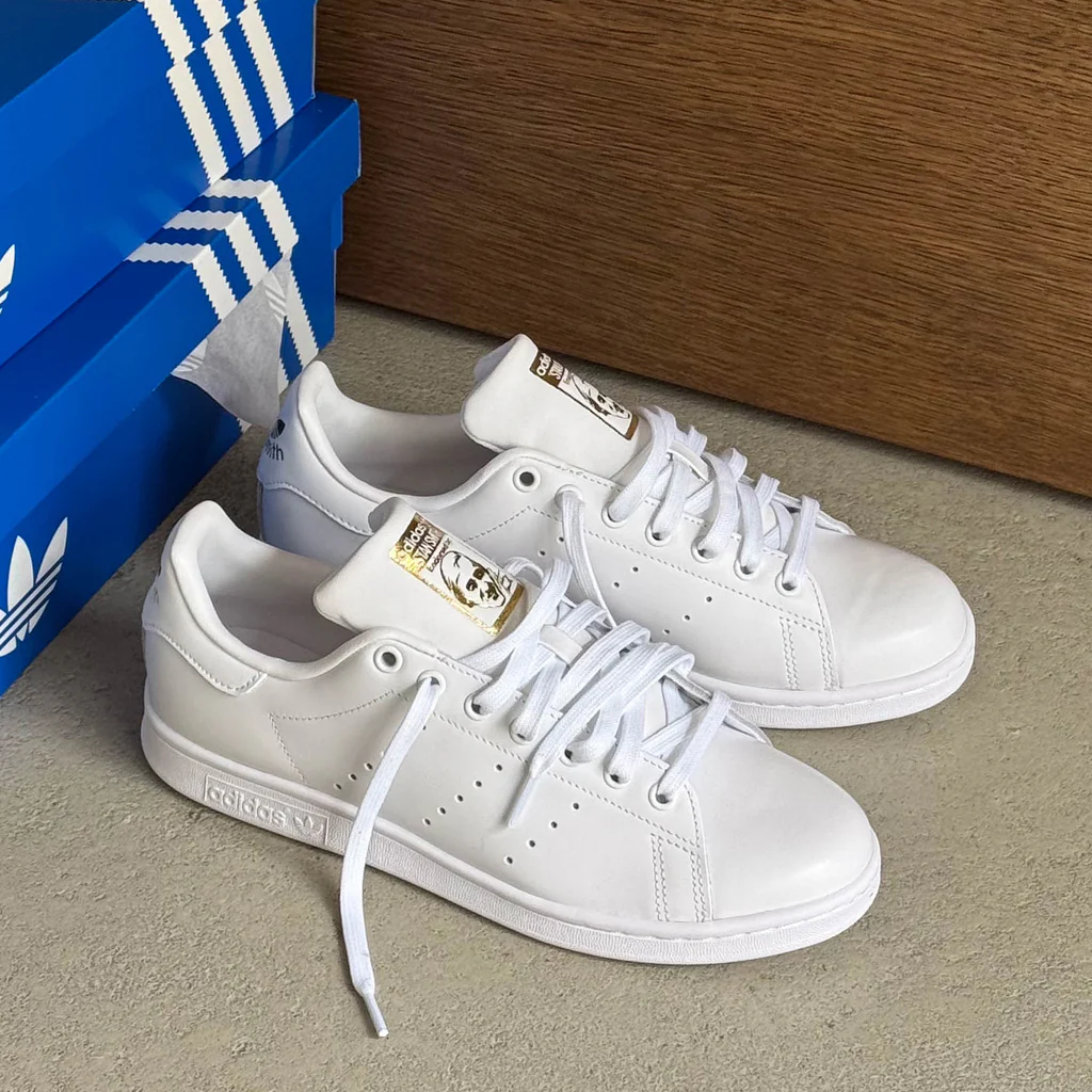 White sneakers next to blue Adidas shoeboxes on a flat surface.