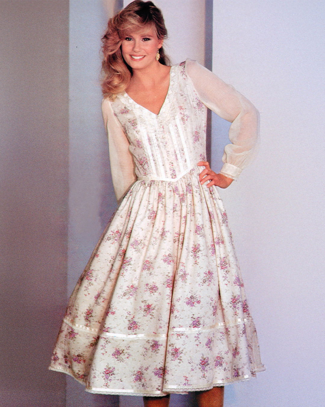 Woman smiling in a floral dress with long sleeves.
