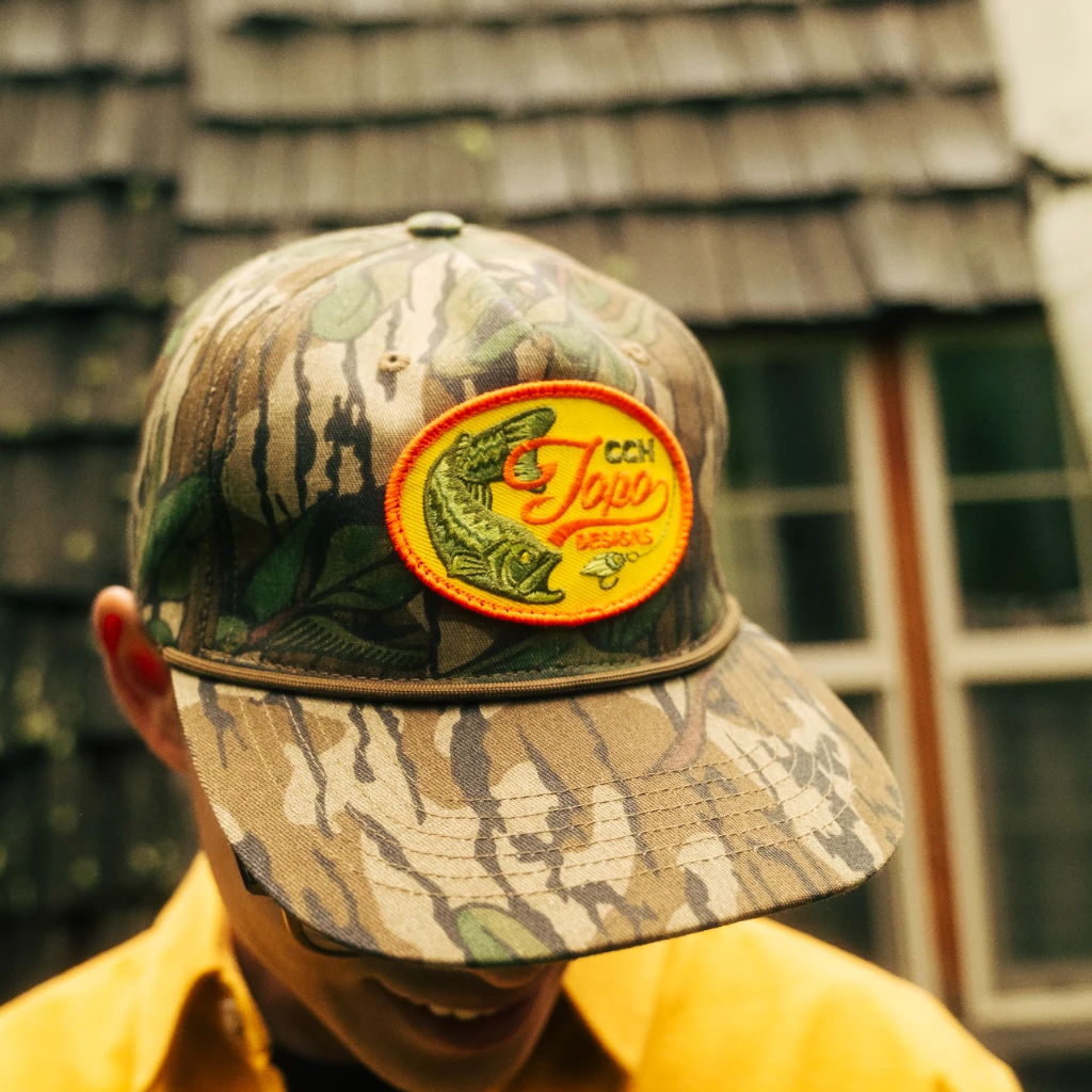 Person wearing a camouflage cap with a fish logo.