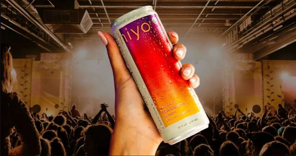 A hand holding a colorful beverage can at a concert.