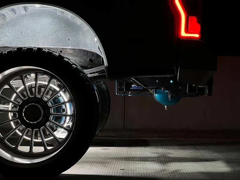 Close-up of Holden's Ford F250 rear wheel at night with LED ring lights and teal air tank