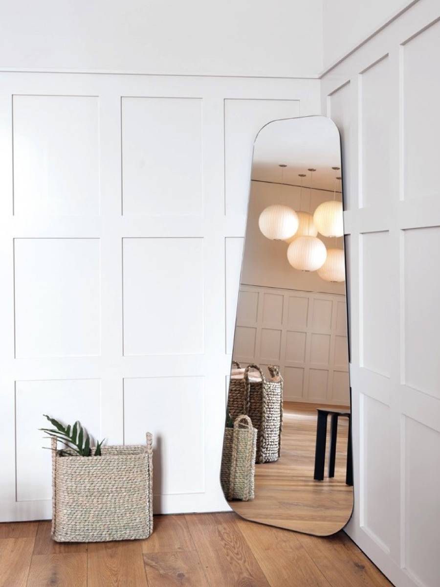 A modern Lean mirror by Schönbuch reflecting a bright, minimalistic interior with woven baskets.