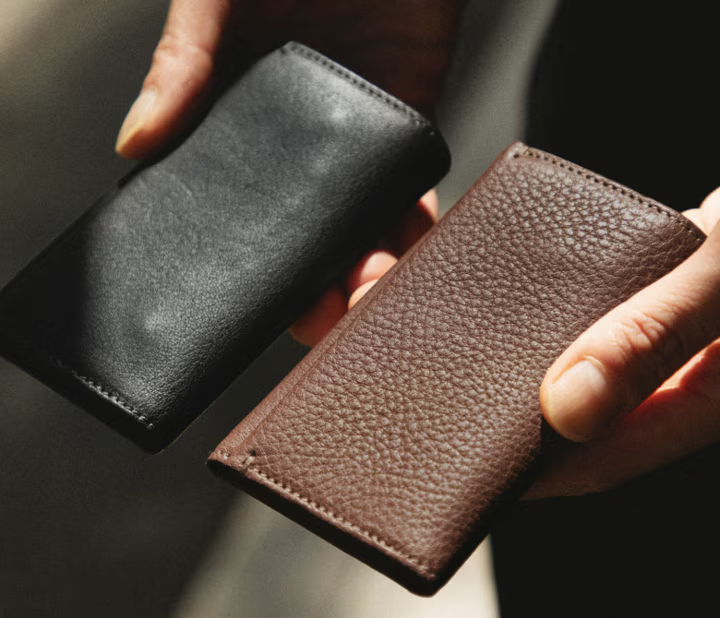 Two leather wallets, one black and one brown, held in hands.