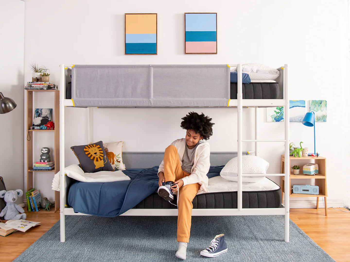 a young boy sitting on the edge of a puffin big kids bed tying his shoes