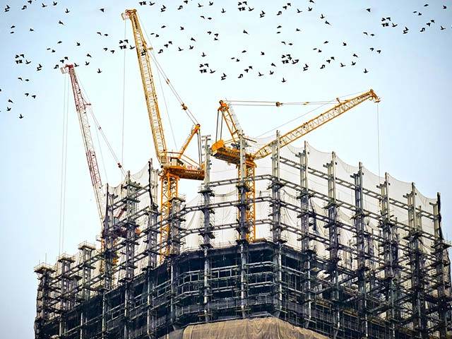 A high building under construction with three cranes