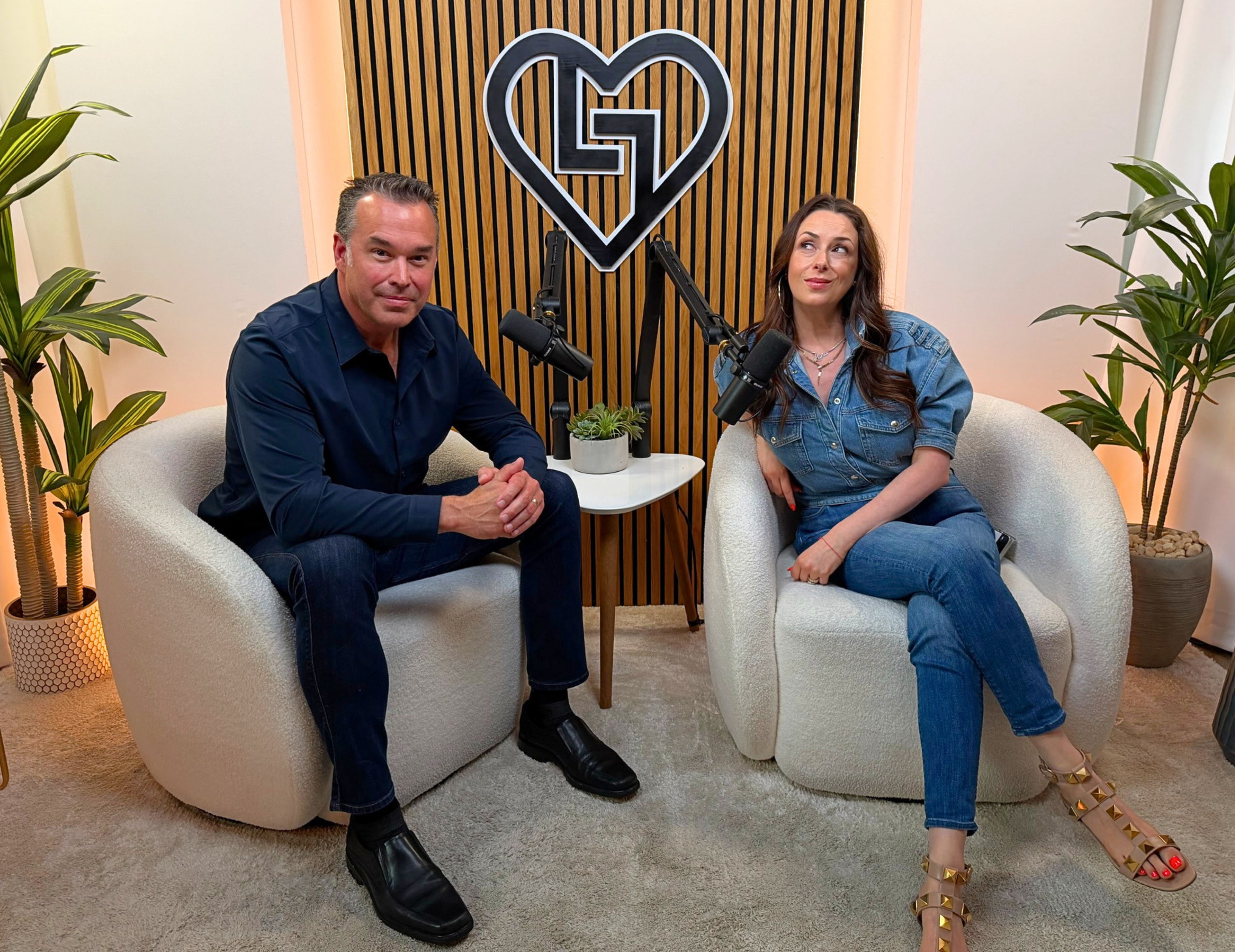 Two people sitting in cozy chairs, with plants and a logo backdrop.