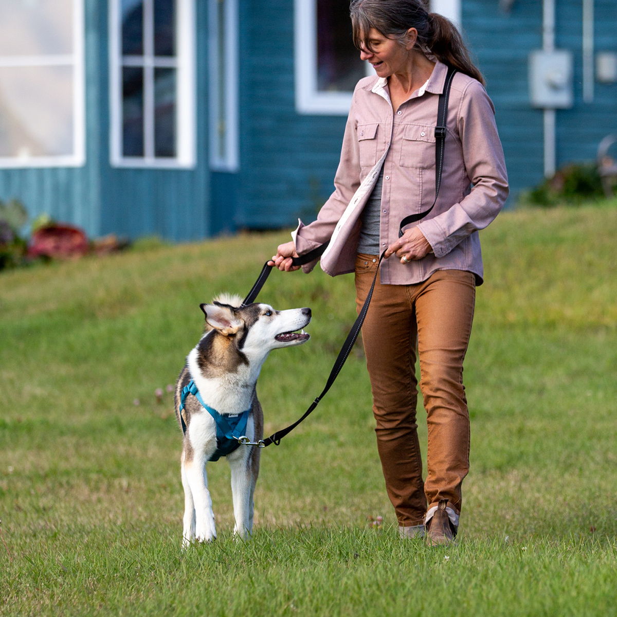 Woman walking a dog on a leash in a grassy area.