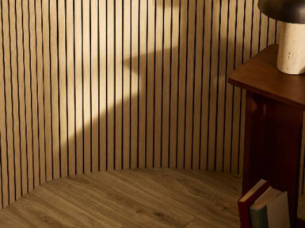 DJH Ultraflex Oak on a curved wall in a corner of a room with a lamp and books, casting shadows.