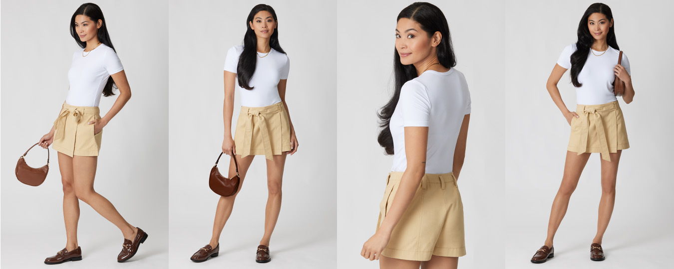 Woman in a white top and beige shorts, posing with a handbag.