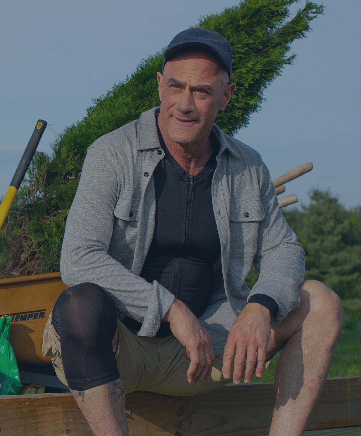 Christopher Meloni doing yard work wearing the Full Back Support Shirt and Compression Knee Sleeve