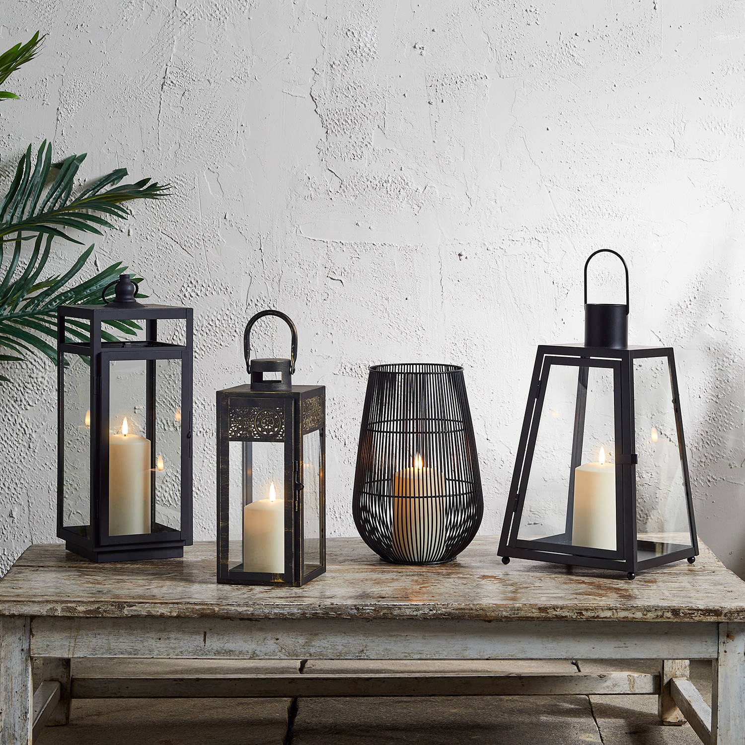 A selection of black garden lanterns in different styles with LED candles inside, sat on a wooden table