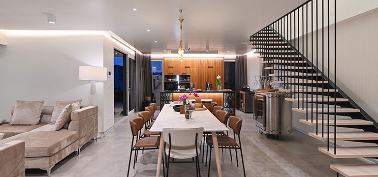 Modern dining area with stairs, couch, and stylish kitchen in background.