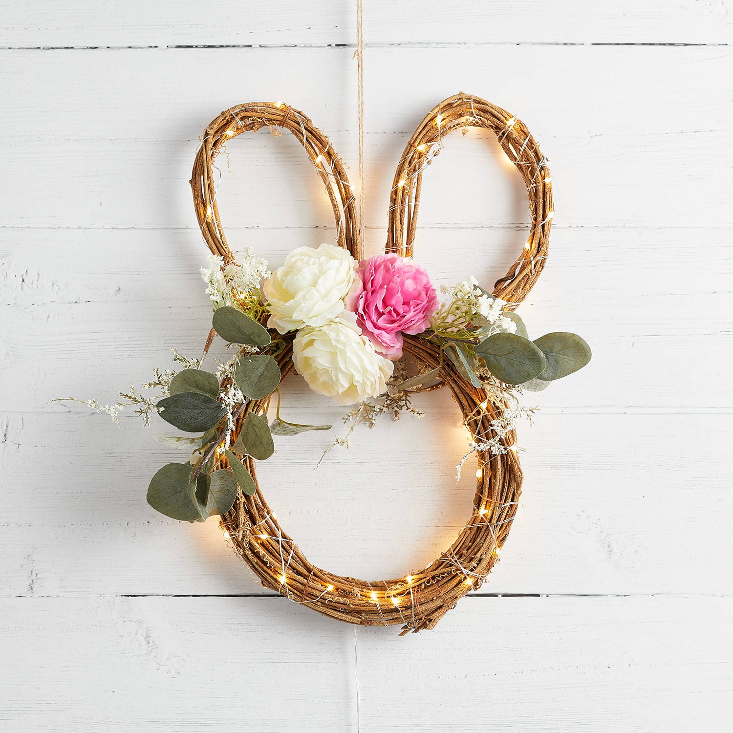 Bunny Easter wreath with foliage and flowers on a white wall with micro lights.