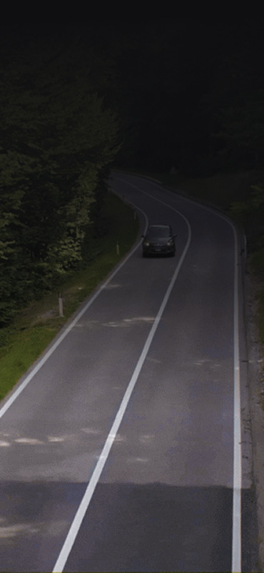 A winding road with a single car driving through a dark forested area.