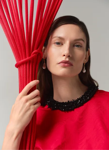 Woman in a red top holding red ropes with a neutral expression.