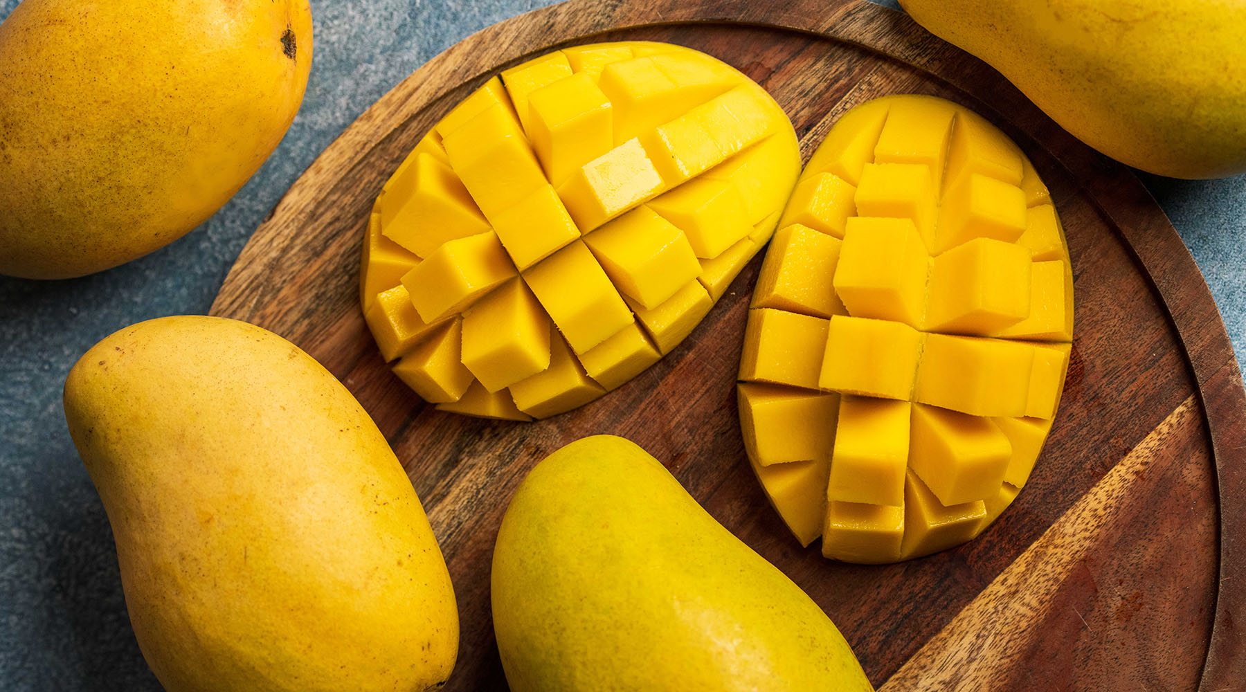 Sliced mangoes and whole mangoes on a wooden cutting board.