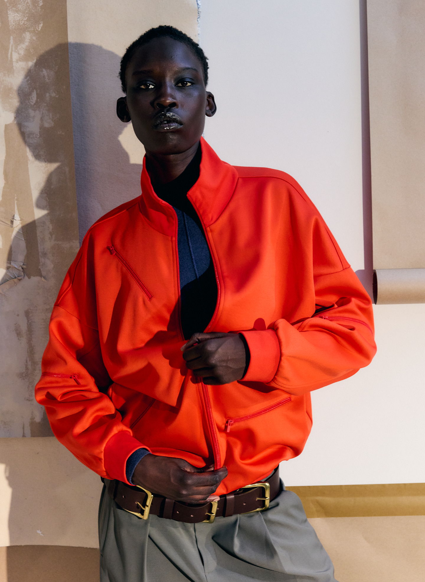 Person wearing an orange jacket and gray pants, posing against a neutral background.