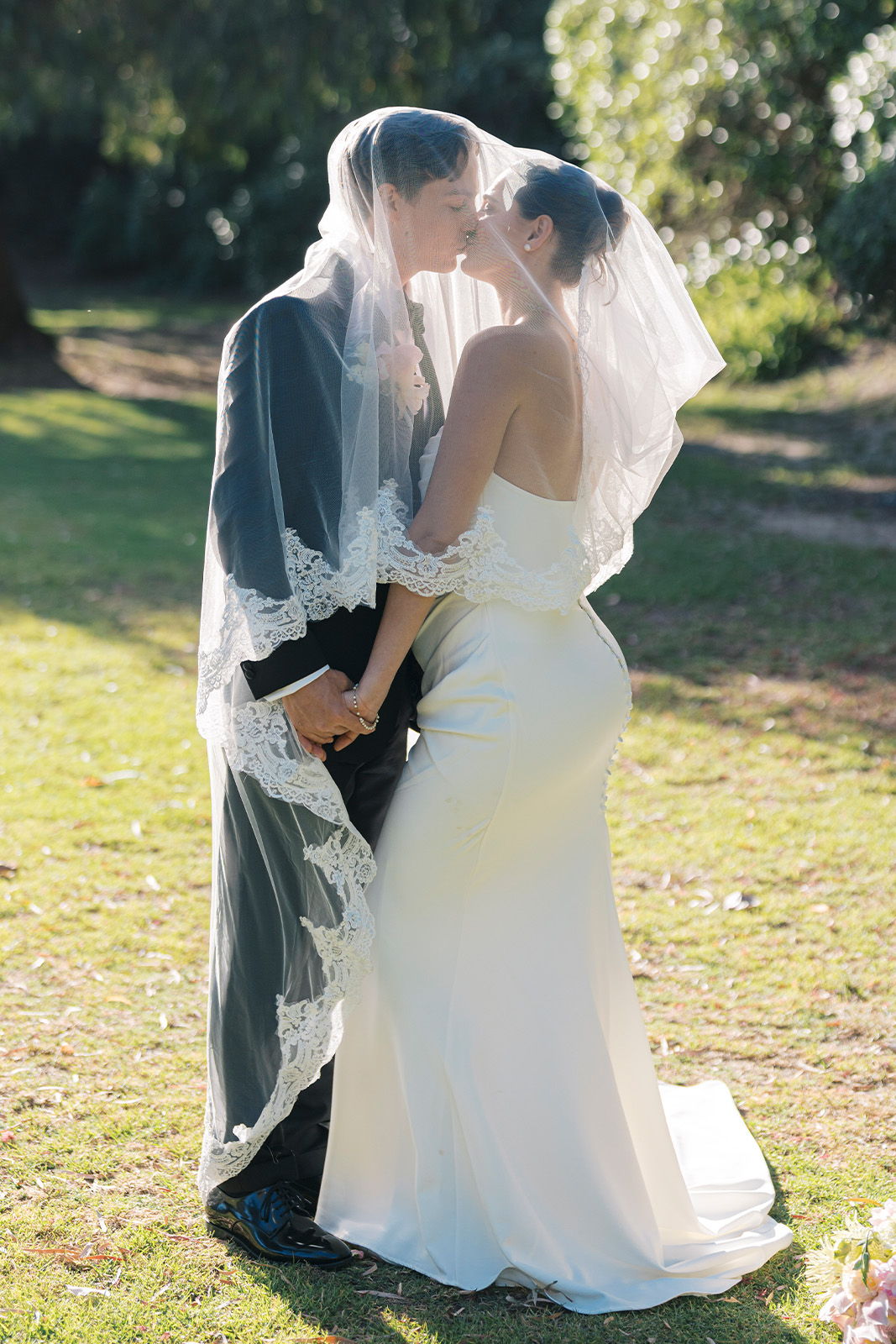 A couple in wedding attire sharing a kiss outdoors.