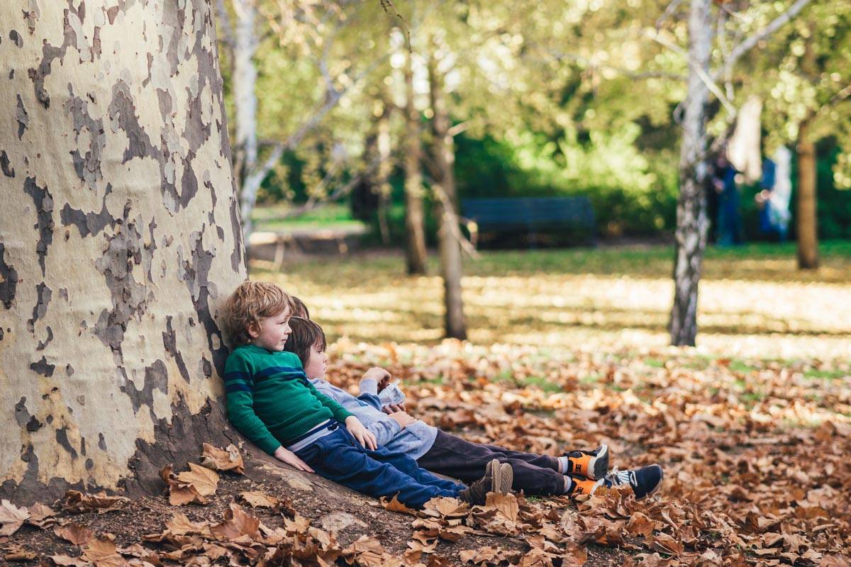 Kids leaning against a tree, surrounded by leaves on the ground