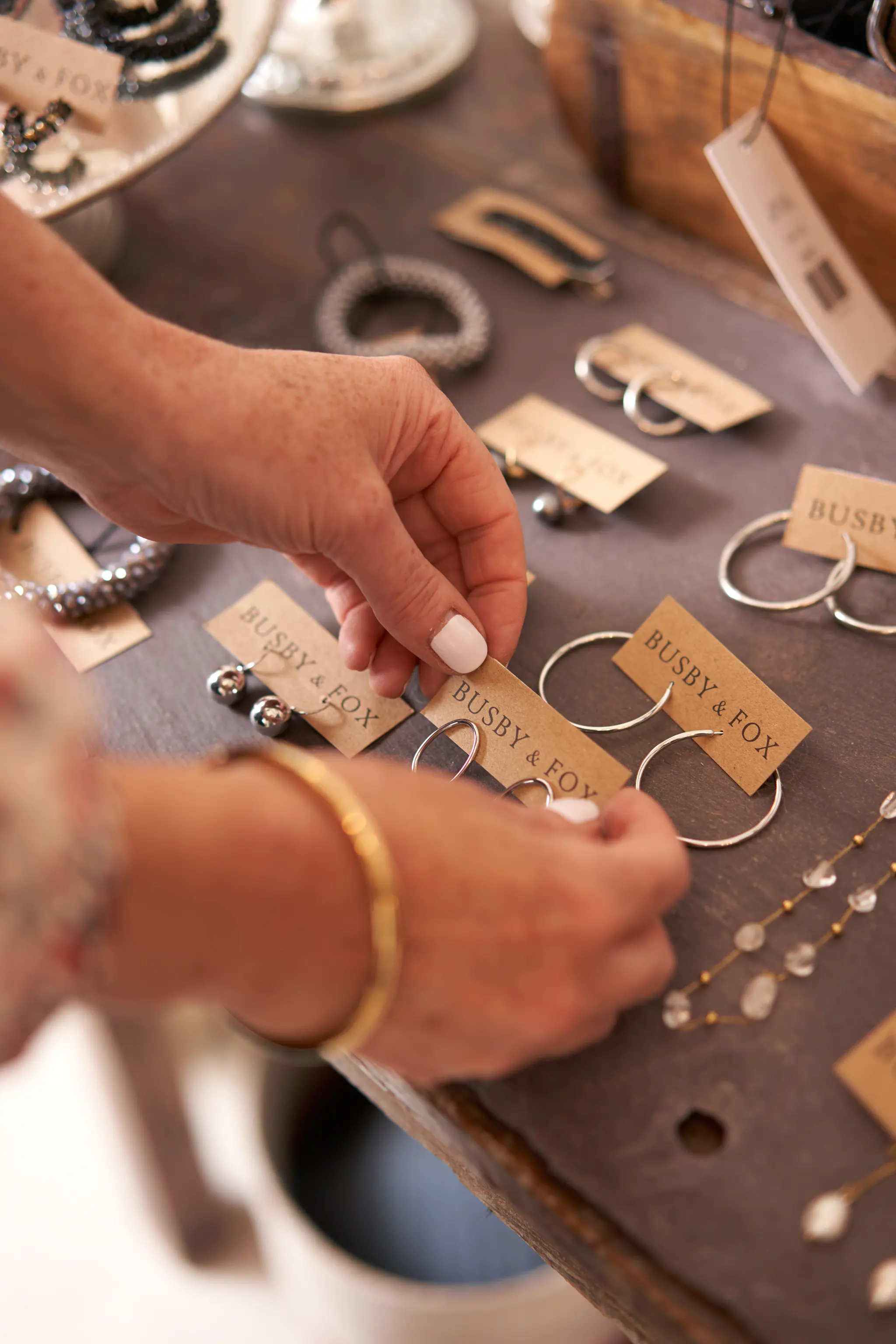 Close up of woman holding a pair of earrings, chosen from a table filled with jewellery