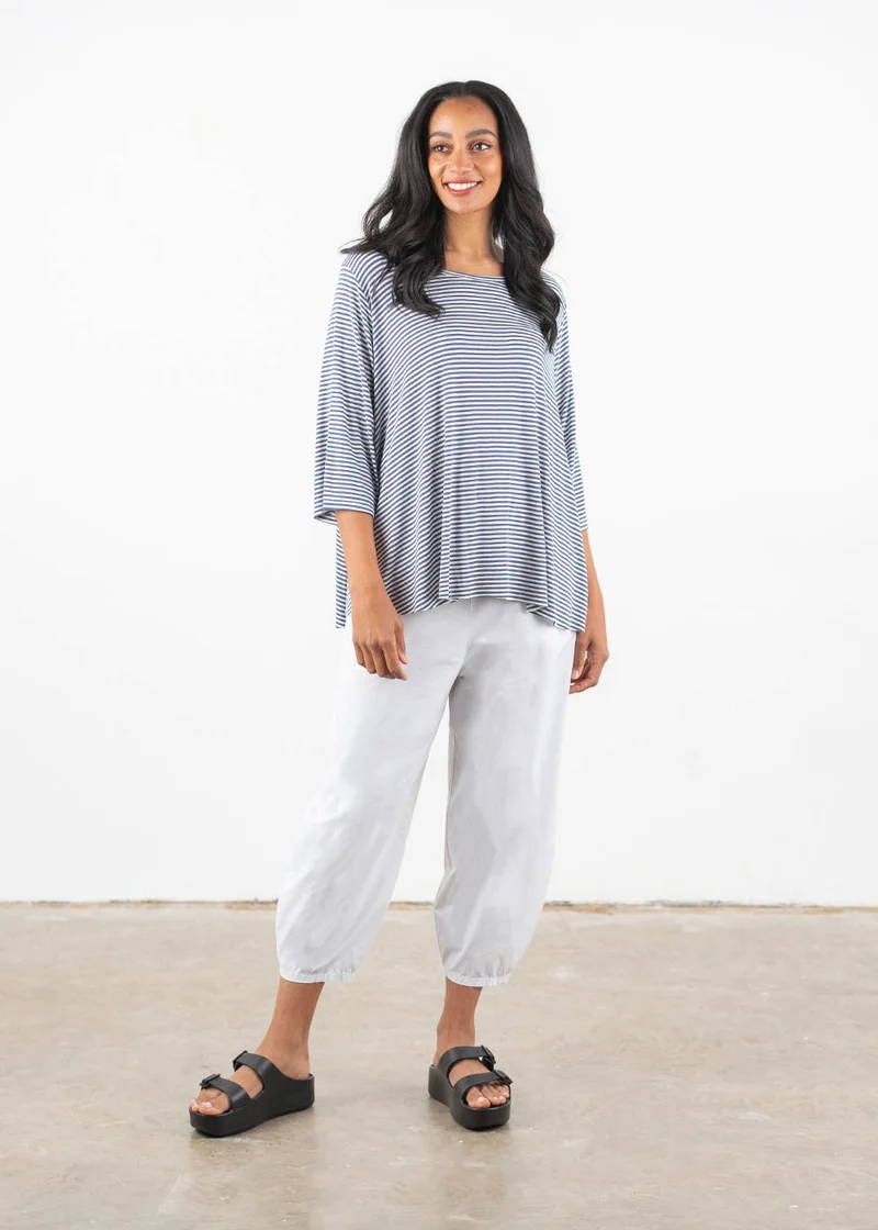 A model wearing a blue and white slouchy 3/4 sleeve top with white balloon leg tapered cotton trousers and black chunky platform slides