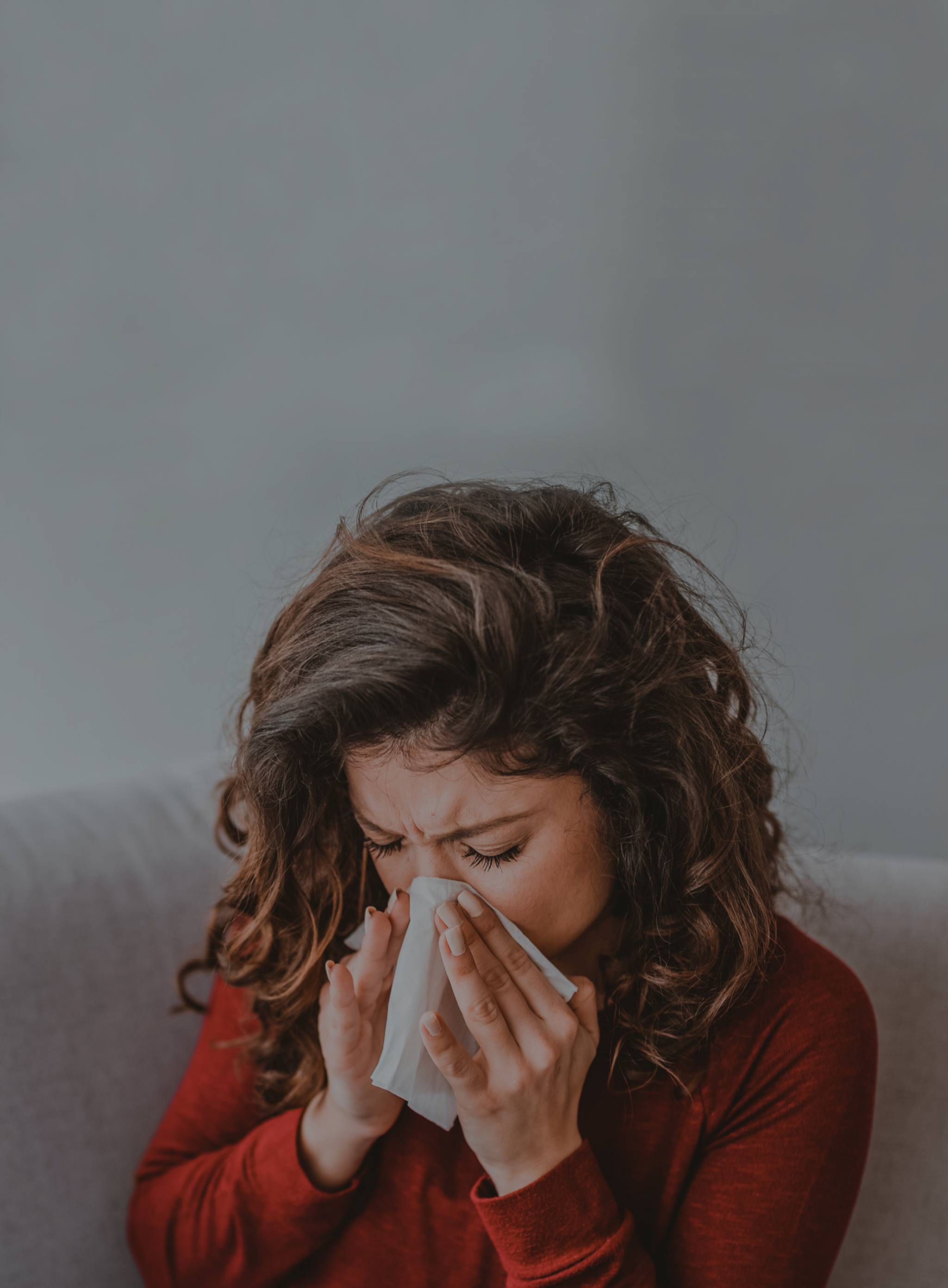 Eine braunhaarige Frau lehnt sich vor und putzt ihre Nase - Bei Allergien kann gleichzeitig eine verstopfte und laufende Nase auftreten.