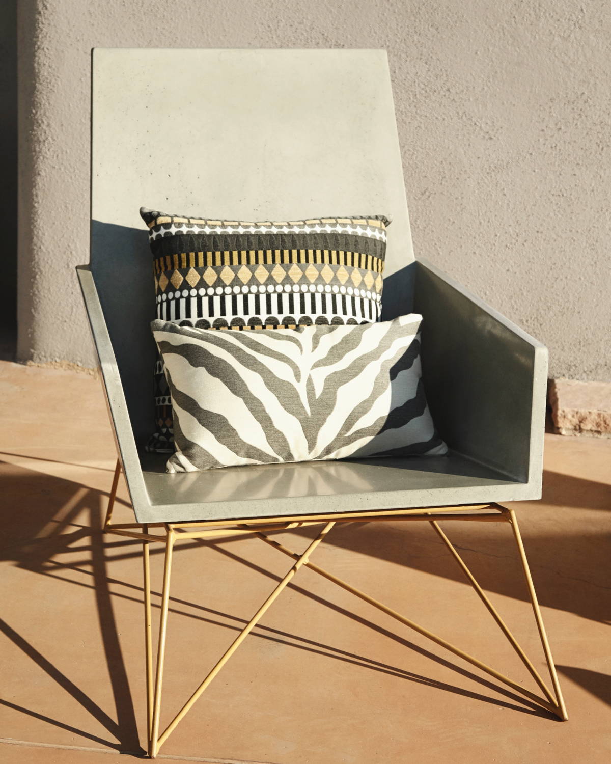 The Modern Muskoka Concrete Lounge Chair in dramatic shadow with geometric pillows.