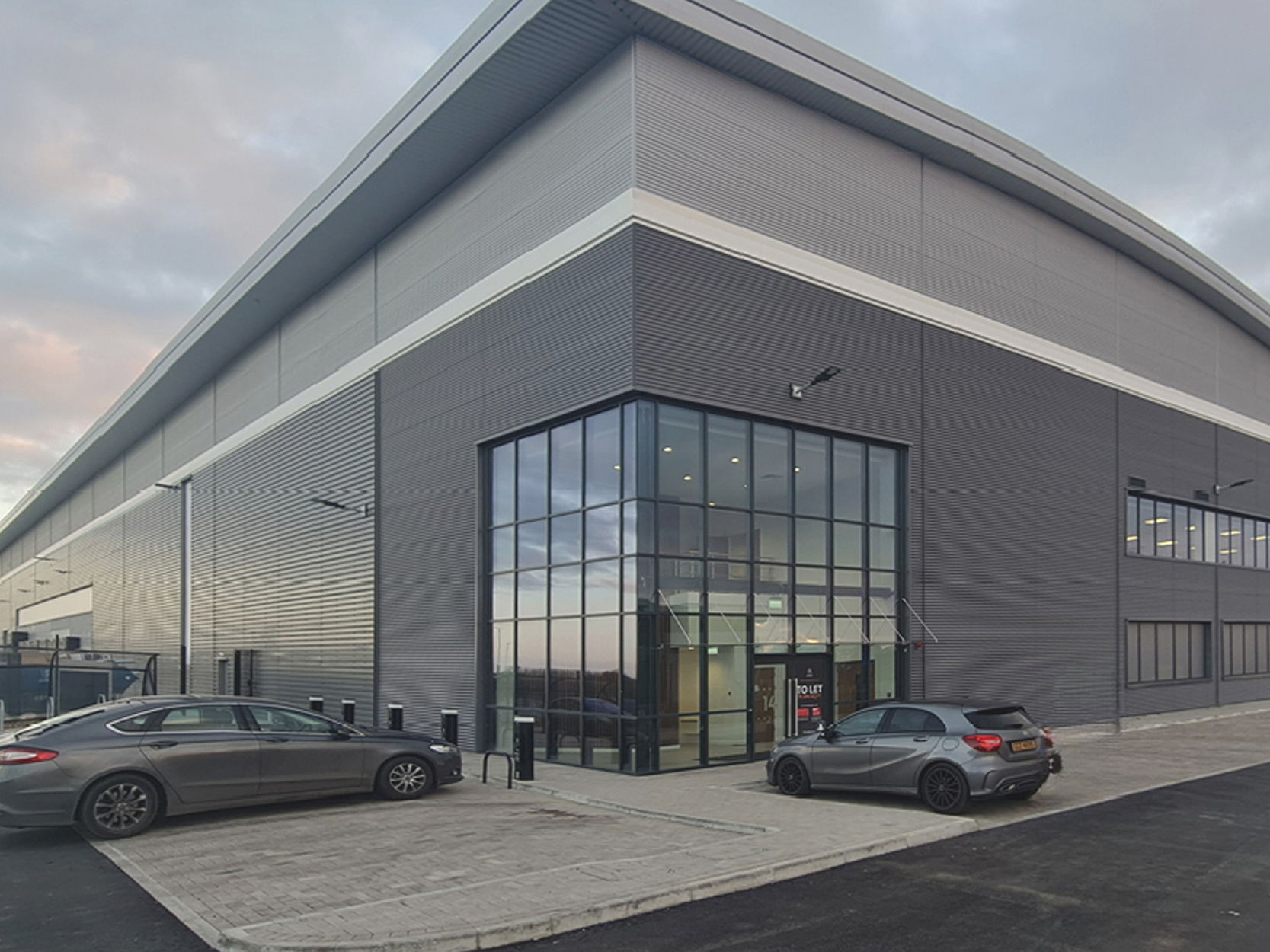 Modern industrial building with large glass entrance and surrounding parking area.